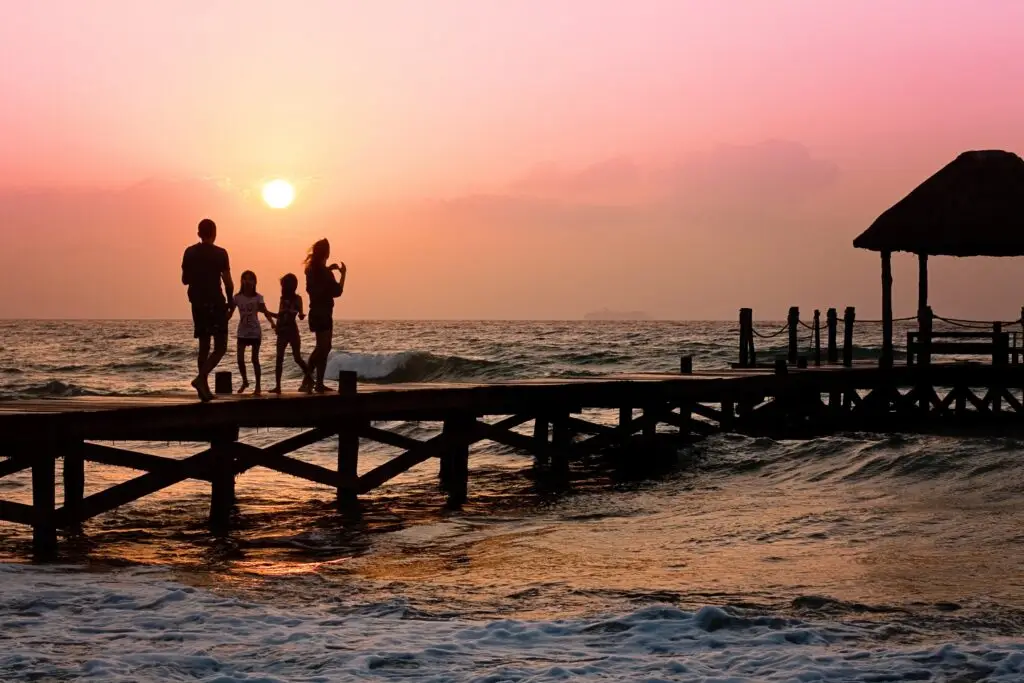 About Us Family walking on pier at sunset.